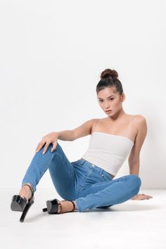 Woman in a white tank top and blue jeans sitting on a white background