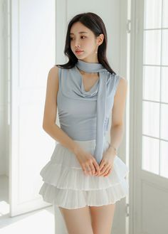 Woman with long dark hair wearing a light blue top and white tiered skirt indoors