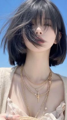 Woman with short black hair and layered gold necklaces against a blue sky