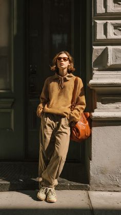 Person in a brown hoodie and baggy pants leaning against a building in sunlight