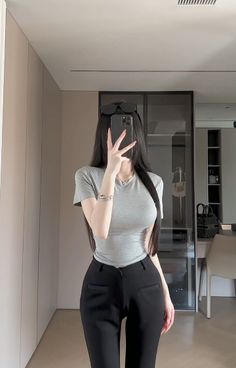 Person with long black hair taking a mirror selfie in a grey t-shirt and black pants
