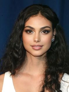 Woman with long dark curly hair and smokey eye makeup against a dark background