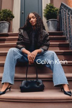 Woman with long hair sitting on outdoor steps, wearing a leather jacket and jeans