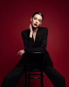 Woman in a black suit with red lipstick posing against a red background