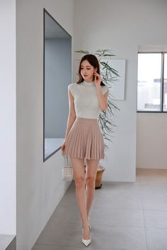 Woman in a white top and pleated mini skirt walking indoors