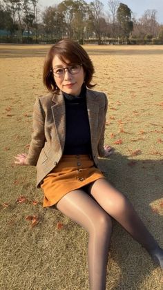Woman with short hair and glasses sitting on grass in a plaid blazer and mini skirt