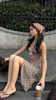 Woman in a plaid dress and head scarf sitting outdoors with a small dog