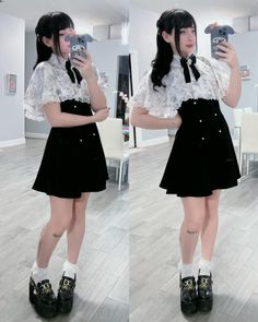 Woman in a black dress and white blouse taking a mirror selfie indoors