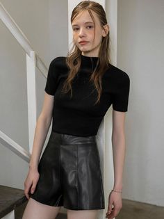 Woman in a black top and leather shorts standing indoors