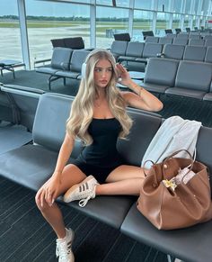 Woman with long blonde hair wearing a black romper and headphones in an airport