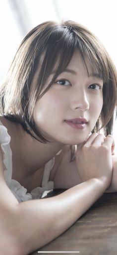 Woman with short brown hair in a white top, resting her chin on her hands