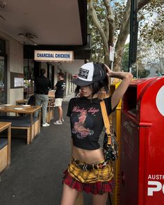 Woman in a plaid skirt and crop top on a street next to a red mailbox