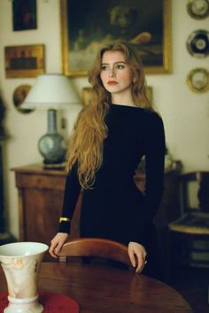 Woman with long red hair in a black dress standing indoors