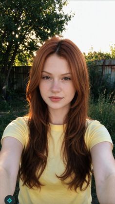 Young woman with red hair and freckles in a yellow t-shirt outdoors at golden hour
