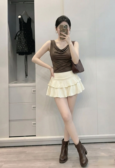 Woman in a brown top and mini skirt taking a mirror selfie indoors