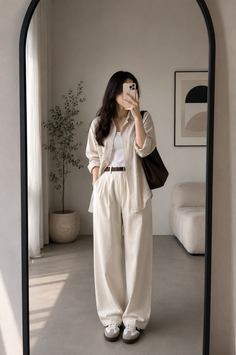 Woman in a loose shirt and wide leg pants taking a mirror selfie indoors
