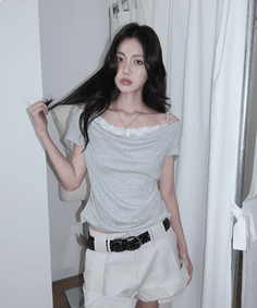 Woman with long dark hair wearing an off-shoulder top and shorts indoors