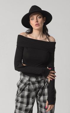 Woman in a black off-shoulder top and plaid pants with a black hat