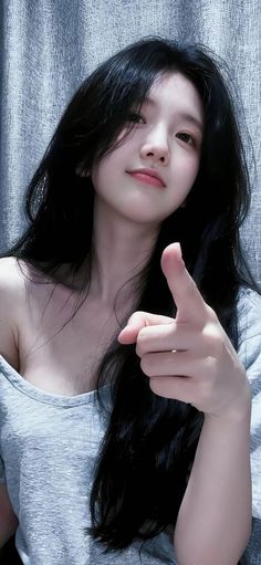 Woman with long black hair in an off-shoulder top pointing at the viewer