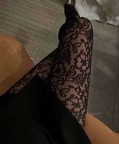 Person wearing black lace tights and a dark skirt while sitting indoors