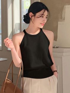 Woman in a black halter top and light pants holding a brown bag indoors