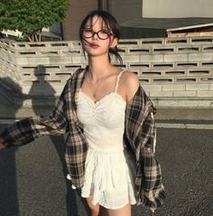 Woman in a plaid shirt and white camisole with glasses outdoors at golden hour