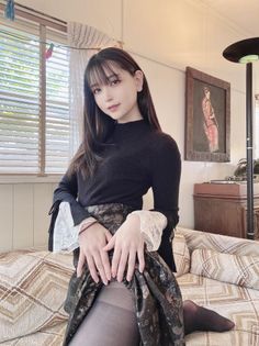 Woman with long hair wearing a black top and patterned skirt indoors