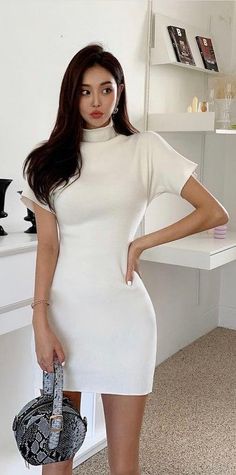 Woman in a white dress holding a snakeskin bag indoors