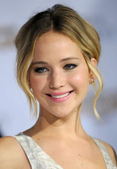 Woman with blonde hair in an updo, smiling with pink lipstick and pearl earrings