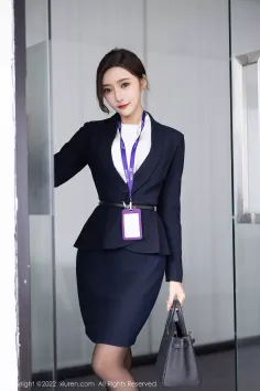 Woman in a dark business suit holding a handbag indoors