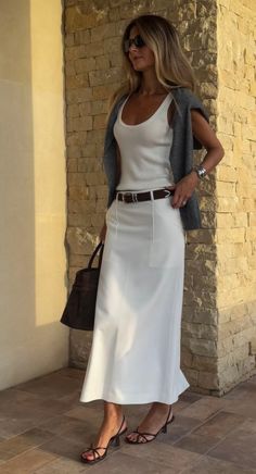 Woman in a white tank top and skirt with a brown belt and bag outdoors