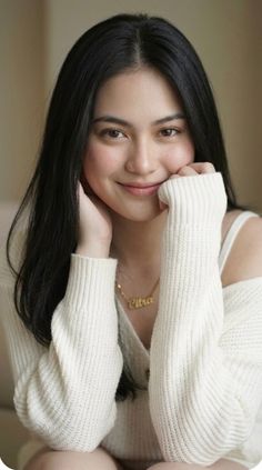 Woman with long black hair wearing a white sweater and gold necklace