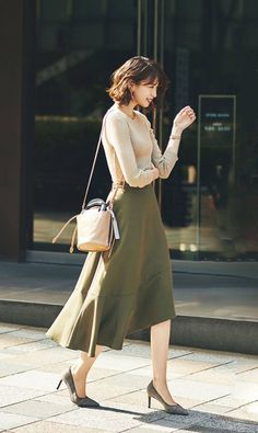 Woman with short hair in an olive skirt and heeled shoes walking outdoors