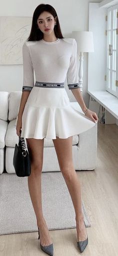 Woman in a white dress and high heels holding a black handbag indoors