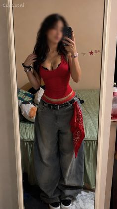 Woman in a red tank top and baggy jeans taking a mirror selfie