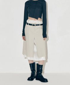 Person in a black cropped top, midi skirt, and black boots against a white background