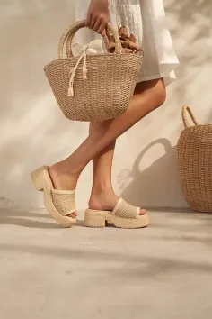 Person in a white dress holding a straw bag and wearing platform sandals