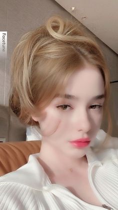 Woman with blonde hair in an updo wearing a white top, with pink lipstick