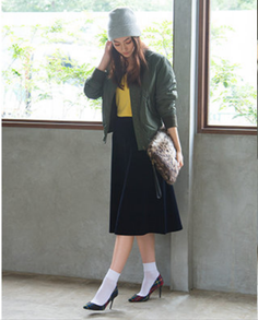 Woman in a beanie, bomber jacket, and midi skirt holding a leopard print bag