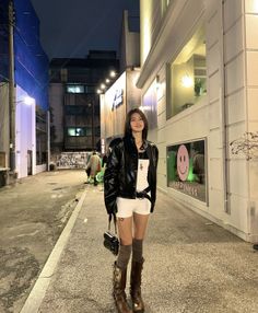Woman in a leather jacket and white shorts on a street at night