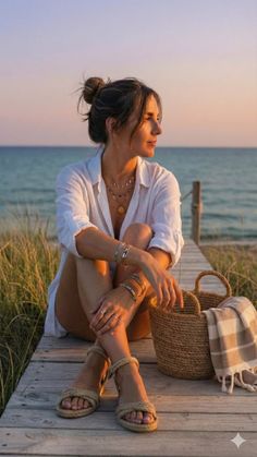 Woman in a white shirt and rope sandals sitting on a wooden pier at sunset