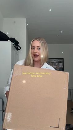 Woman with blonde hair holding a Nordstrom Anniversary Sale haul box indoors