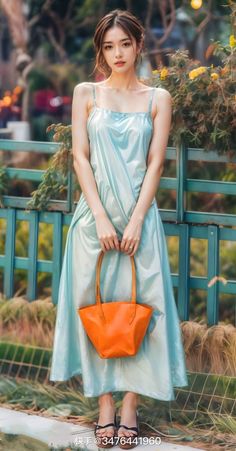 Woman in a light blue dress holding an orange handbag outdoors