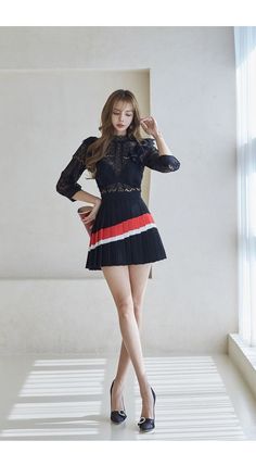 Woman in a black lace top and pleated skirt posing indoors