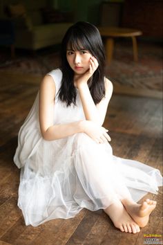 Woman in a white dress sitting on a wooden floor indoors