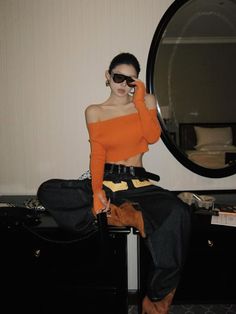 Woman in an orange off-shoulder top and baggy pants sitting on a dresser