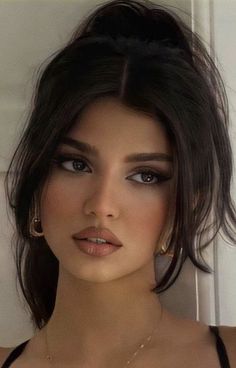 Woman with dark hair in a ponytail and makeup, wearing earrings and a necklace