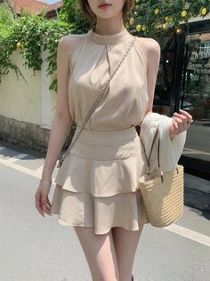 Woman in a beige halter top and tiered skirt holding a straw bag outdoors
