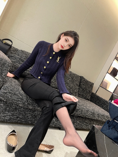 Woman in a dark blue cardigan and black pants with sheer stockings, sitting indoors
