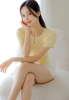 Woman with long dark hair wearing a yellow top and white shorts, sitting indoors